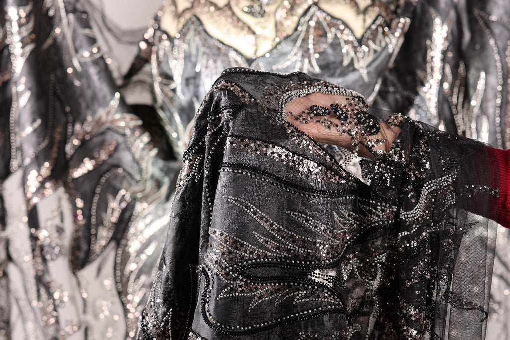 A close-up view of a hand holding a piece of fabric with intricate black and silver sequin designs.