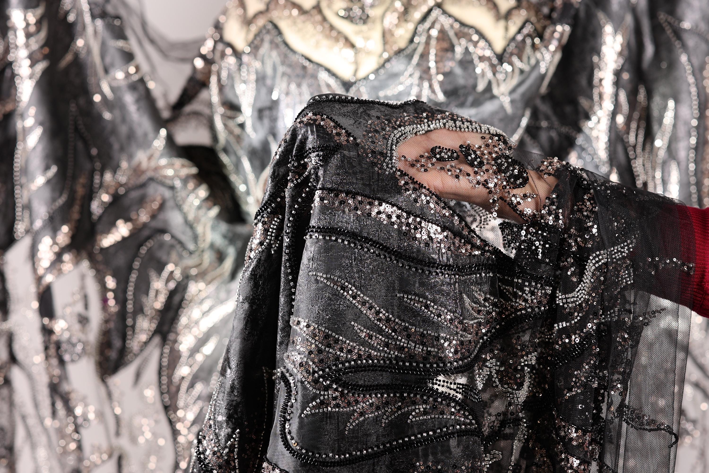 A close-up view of a hand holding a piece of fabric with intricate black and silver sequin designs.