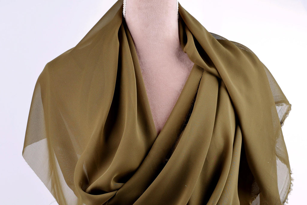 A close-up view of a mannequin wearing a green, draped fabric draped over its torso.