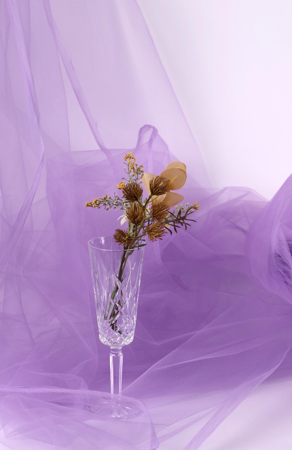A clear glass vase filled with a bouquet of flowers sits on a purple background.