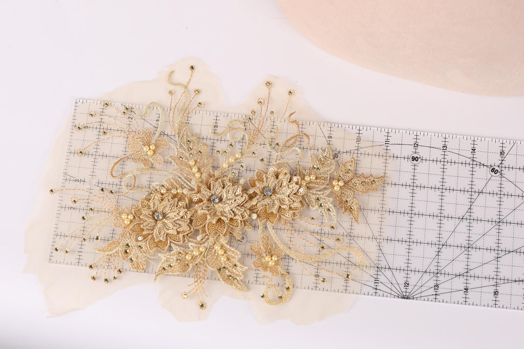 a decorative gold floral piece with intricate details, placed on a transparent ruler against a white background.
