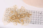 a decorative gold floral piece with intricate details, placed on a transparent ruler against a white background.