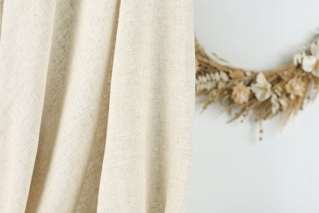 a beige fabric hanging on a wall, with a wreath made of dried flowers placed next to it.