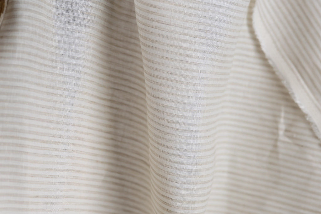 A close-up view of a fabric with horizontal stripes in various shades of white and beige.