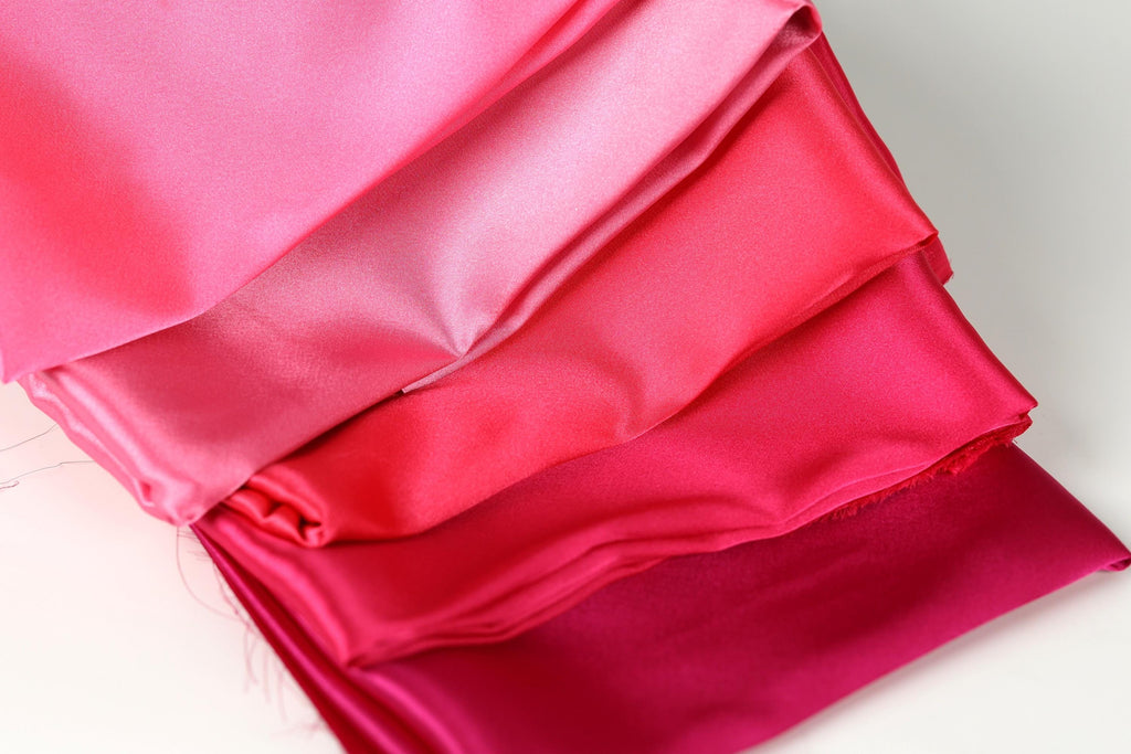 A close-up image of a pile of fabric in various shades of pink, ranging from a soft, pastel pink to a more intense, deep pink.