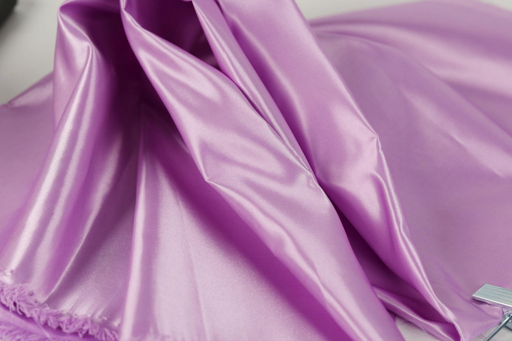 a close-up view of a soft, shiny purple fabric, possibly silk or satin, with a slightly wrinkled texture.
