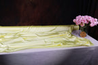 a table with a yellow satin tablecloth, a vase of pink roses, and a dark background.