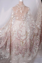 A mannequin wearing a sheer, lace-like fabric with a floral pattern in shades of pink and white.