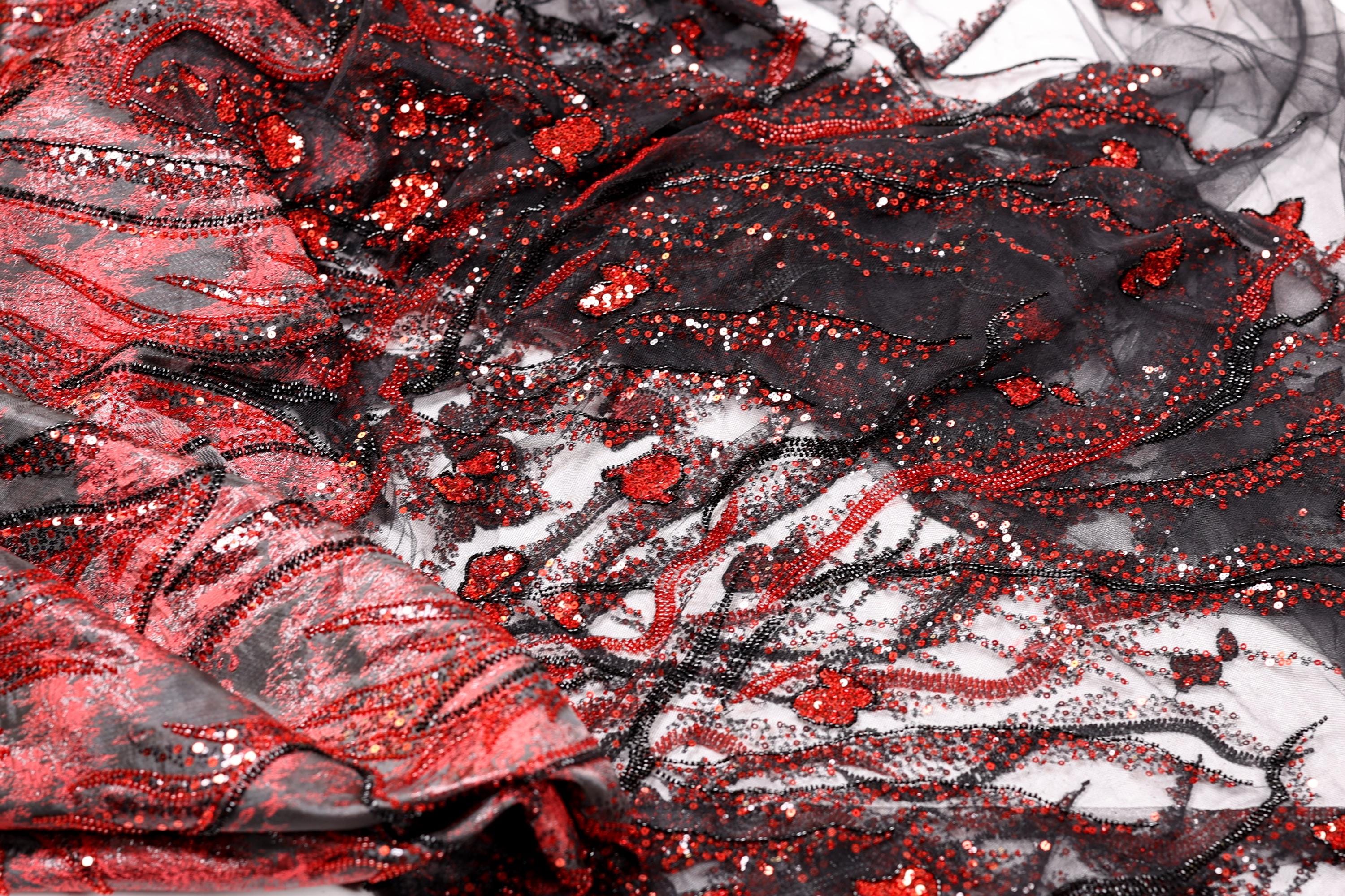 The image is a close-up of a fabric with a striking pattern of red and black sequins and beads, creating a visually captivating and intricate design.