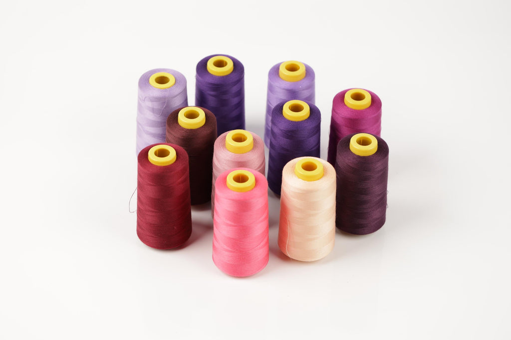 A collection of colorful spools of thread in various shades of purple, pink, and maroon, arranged in a circular pattern on a white background.