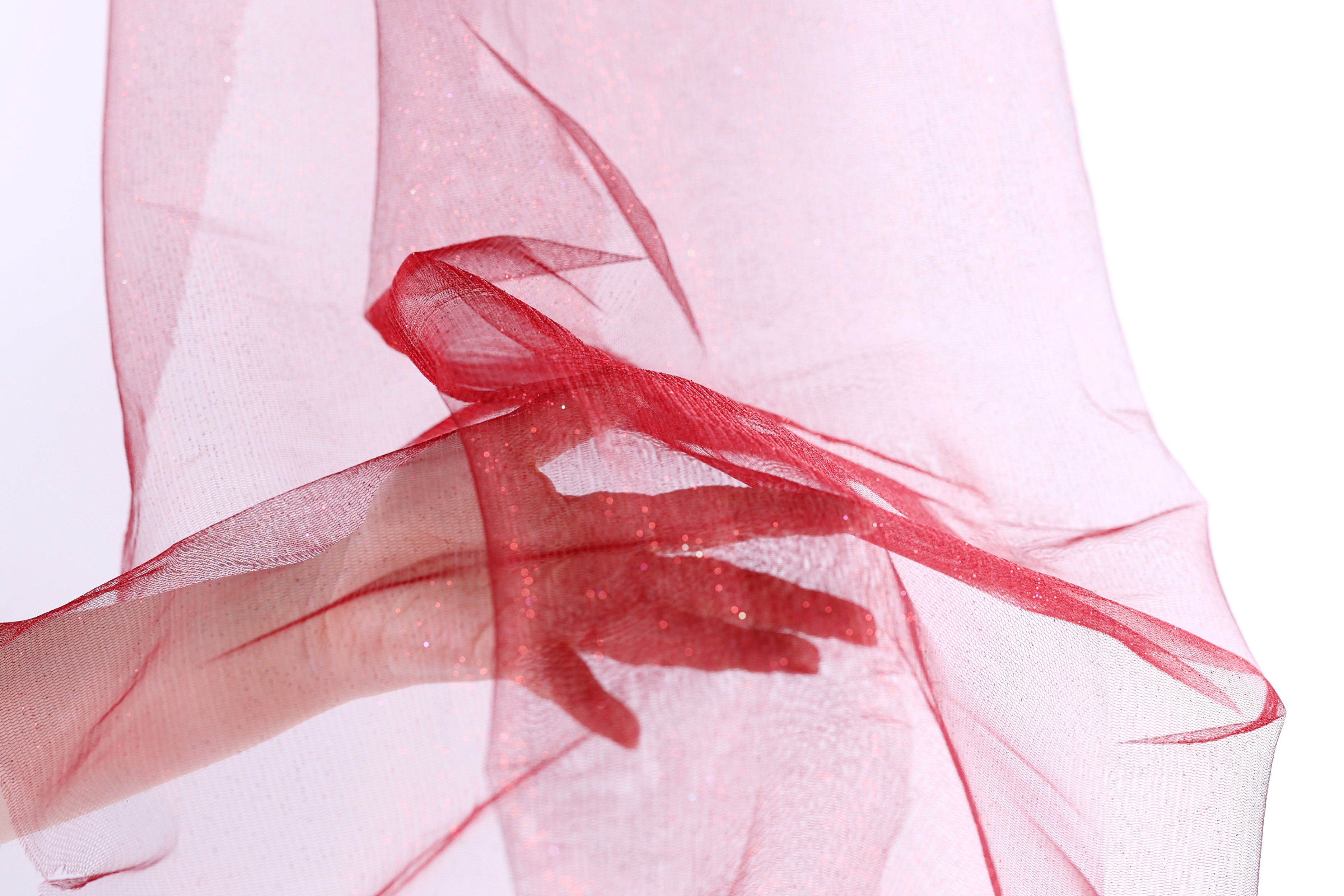 A hand is holding a red, shiny fabric or material, which appears to be a sheer or sheer-like fabric. The hand is positioned in front of the fabric, with the fingers curled around it.