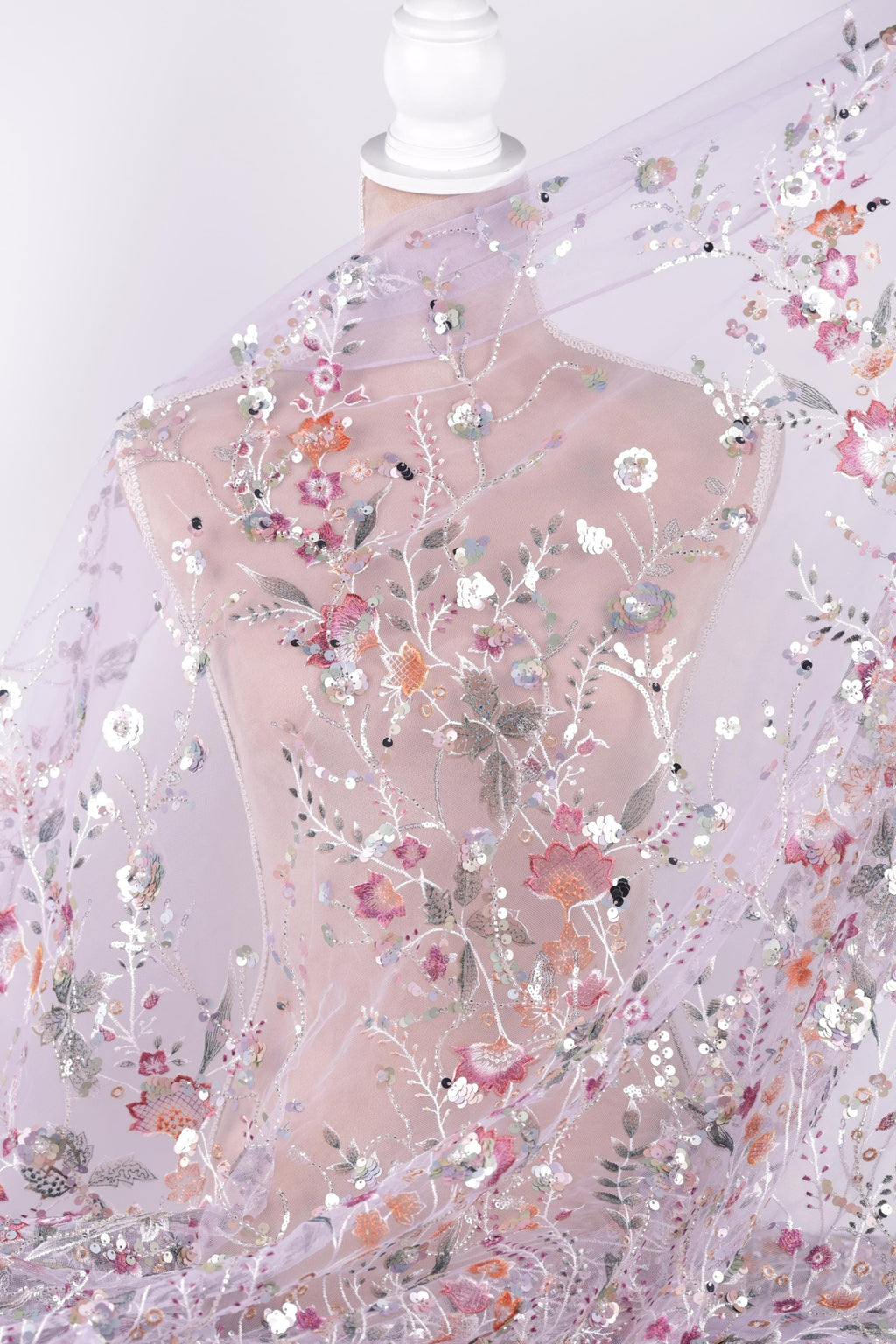 a mannequin wearing a sheer, floral-patterned fabric draped over it. The fabric has a delicate, transparent appearance and is adorned with a variety of colorful flowers and leaves. The mannequin is positioned in a way that allows the fabric to be fully visible, showcasing the intricate details and patterns of the fabric.