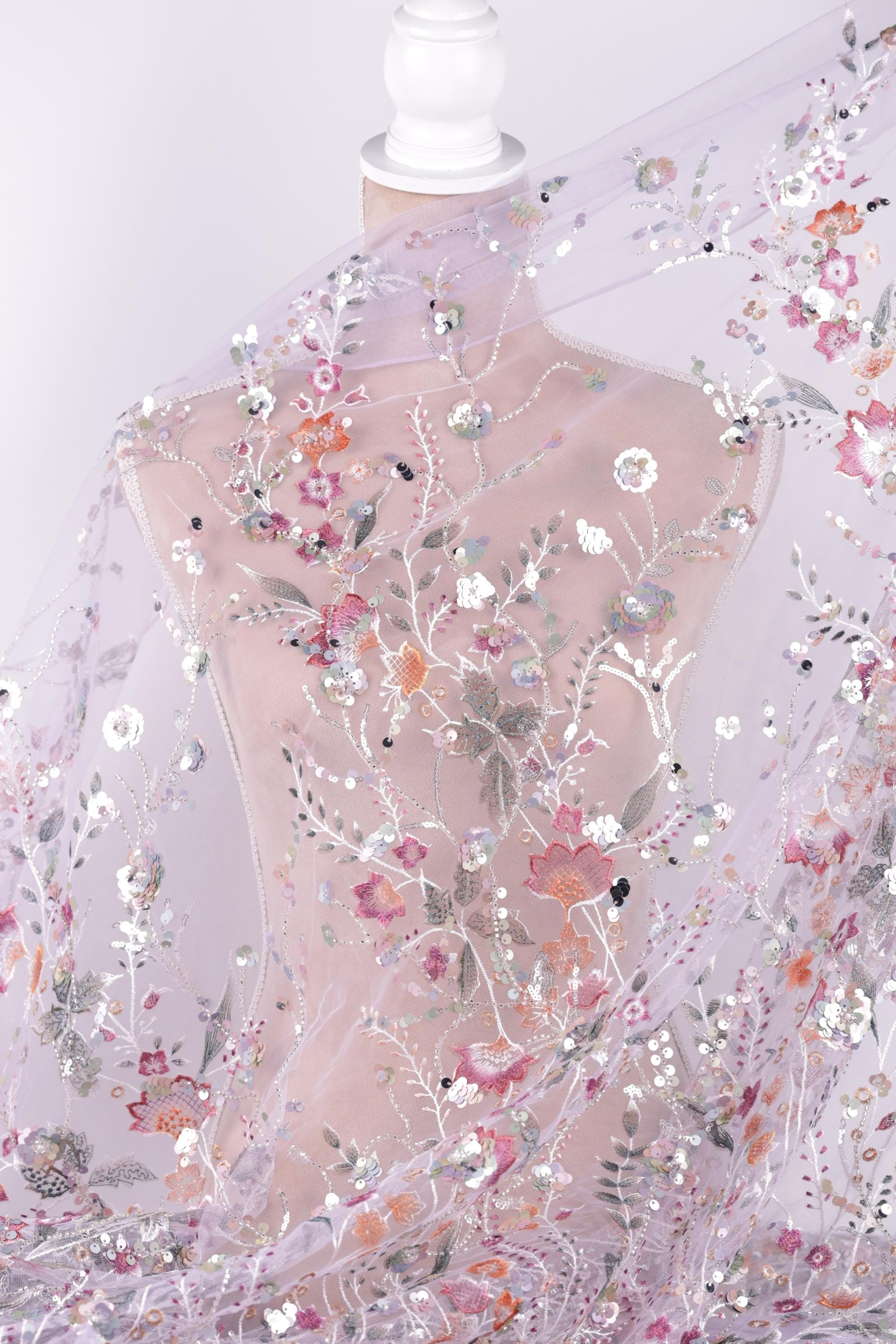 a mannequin wearing a sheer, floral-patterned fabric draped over it. The fabric has a delicate, transparent appearance and is adorned with a variety of colorful flowers and leaves. The mannequin is positioned in a way that allows the fabric to be fully visible, showcasing the intricate details and patterns of the fabric.