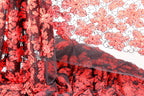 a close-up view of a fabric with a striking red and black floral pattern. The fabric appears to be a sheer material, with a black lace-like texture that adds an elegant touch to the design. The pattern is intricate and detailed, showcasing the craftsmanship and artistry involved in creating this textile.