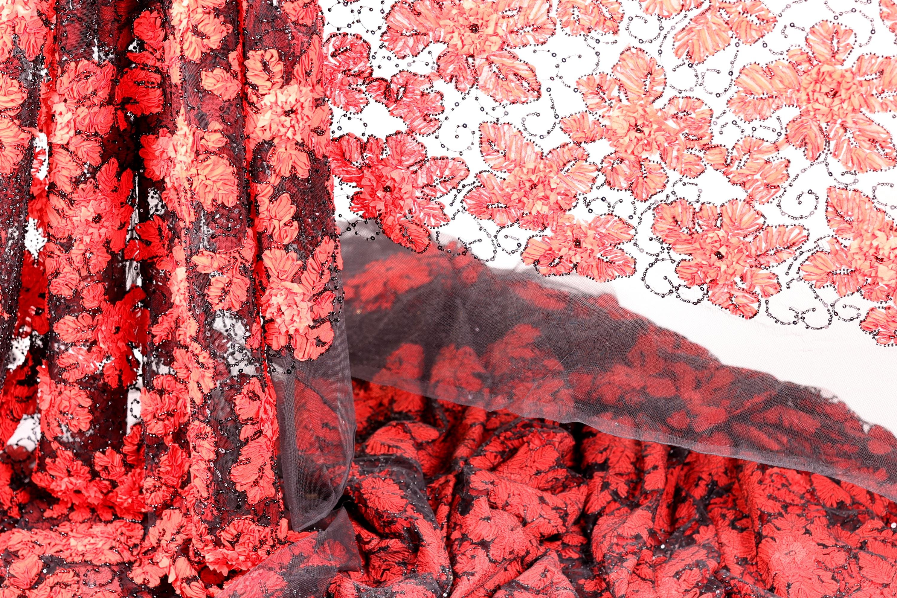 a close-up view of a fabric with a striking red and black floral pattern. The fabric appears to be a sheer material, with a black lace-like texture that adds an elegant touch to the design. The pattern is intricate and detailed, showcasing the craftsmanship and artistry involved in creating this textile.