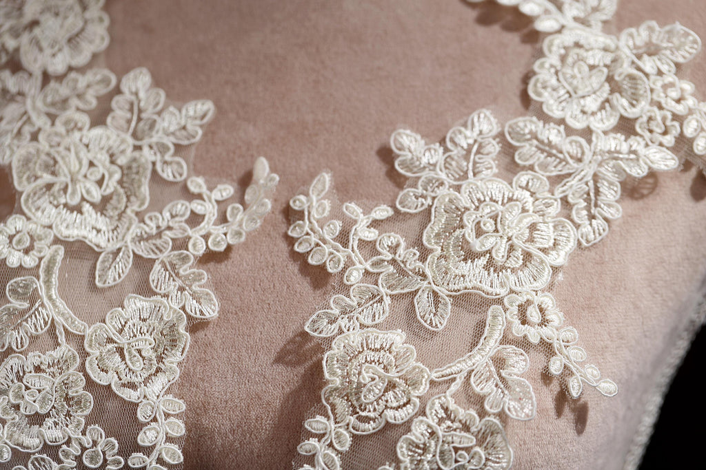 A close-up view of a delicate, intricate white lace pattern on a fabric surface.