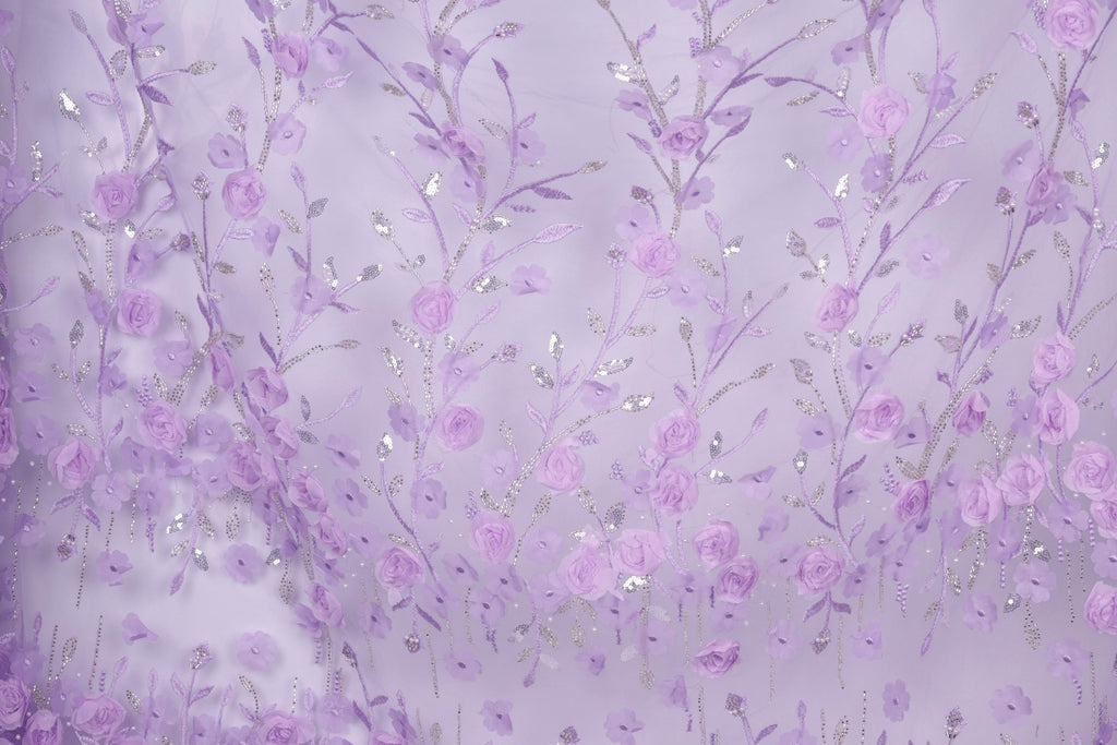 a close-up view of a fabric with a delicate floral pattern in shades of purple and white. The fabric appears to be made of a sheer material, with numerous small flowers and leaves intricately woven into the design. The overall color scheme of the fabric is predominantly purple, with accents of white and silver adding depth and contrast to the pattern.