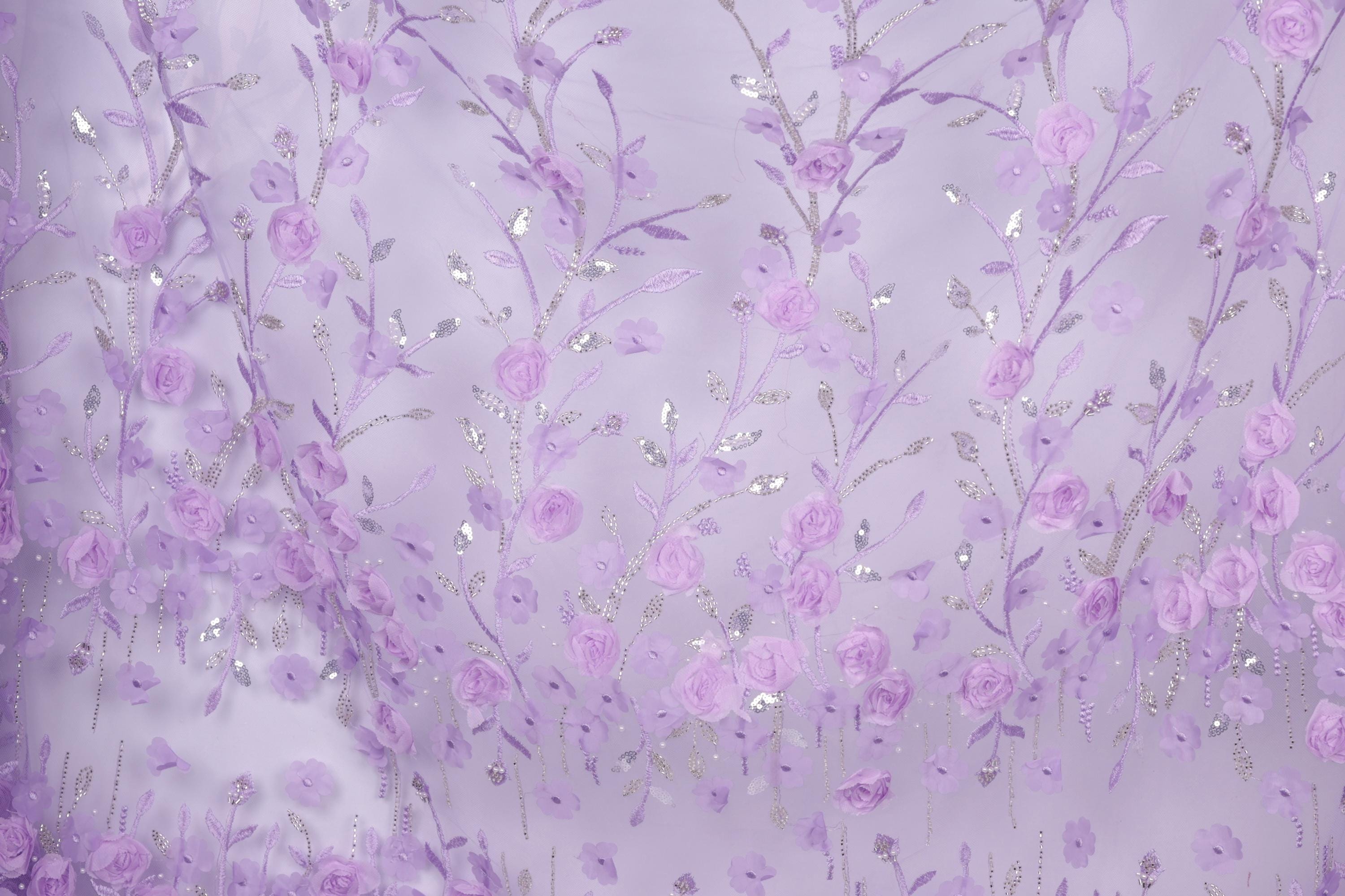 a close-up view of a fabric with a delicate floral pattern in shades of purple and white. The fabric appears to be made of a sheer material, with numerous small flowers and leaves intricately woven into the design. The overall color scheme of the fabric is predominantly purple, with accents of white and silver adding depth and contrast to the pattern.
