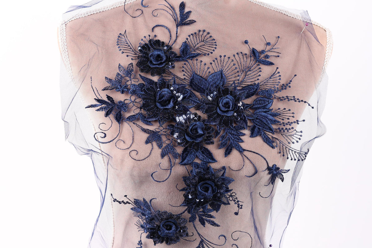 a close-up view of a delicate, intricate blue floral embroidery on a fabric, with the flowers and leaves appearing to be made of lace.