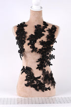A mannequin bust is adorned with black lace, featuring intricate floral and leaf patterns. The lace is sewn onto the bust in a decorative manner, creating a striking contrast against the light-colored fabric.