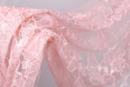A close-up view of a delicate, pink lace fabric with intricate floral patterns.