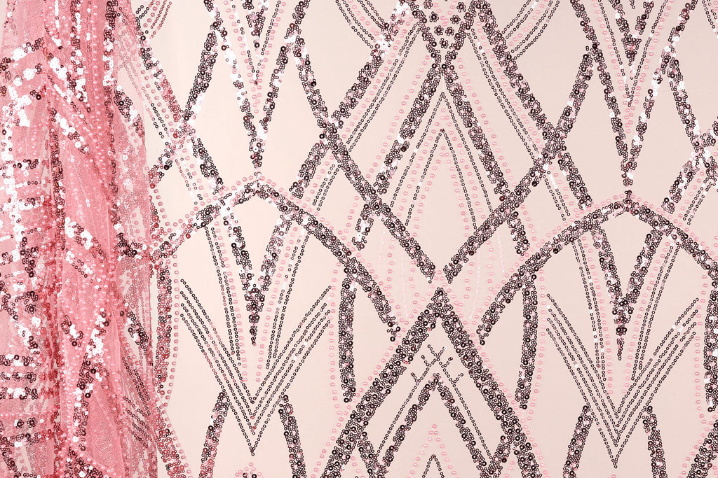 a close-up view of a fabric with a pink and black sequin pattern. The fabric appears to be a sheer material, with the pink sequins creating a visually striking contrast against the light-colored background. The pattern consists of various shapes and lines, including triangles, diamonds, and arches, which contribute to the overall design and texture of the fabric.