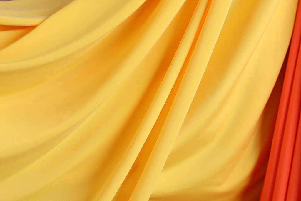 The image is a close-up of a yellow and red fabric, with the fabric appearing to be folded or draped in a way that creates a sense of movement and texture.