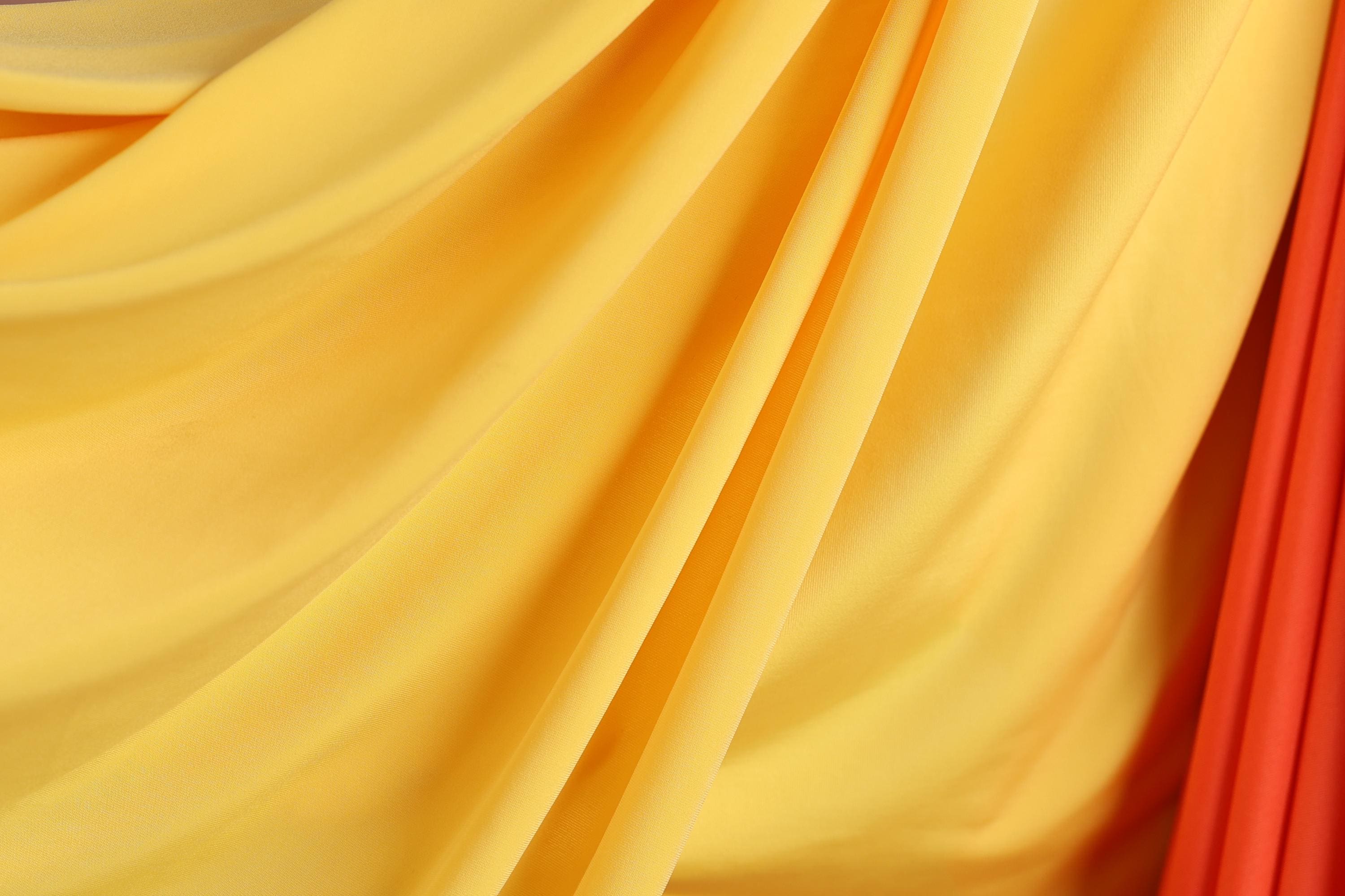 The image is a close-up of a yellow and red fabric, with the fabric appearing to be folded or draped in a way that creates a sense of movement and texture.