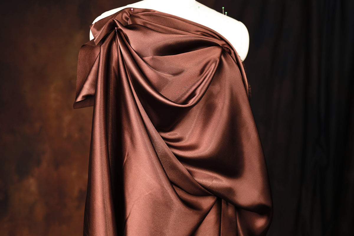 A mannequin wearing a brown satin dress with a draped, flowing silhouette.
