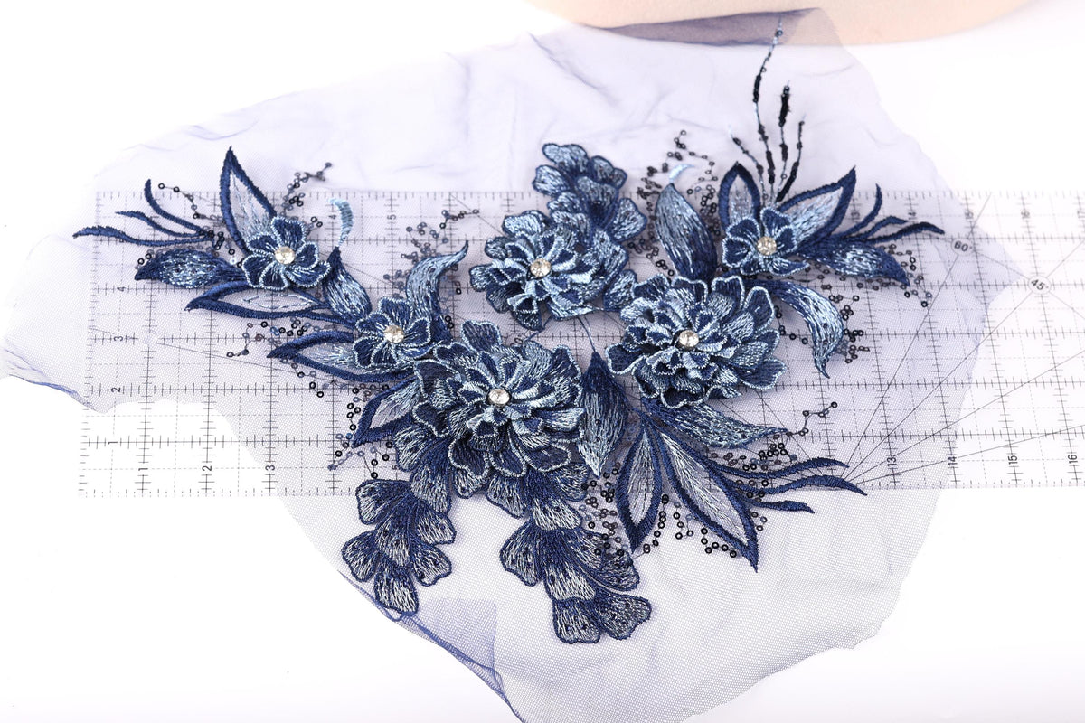 a close-up view of a delicate blue floral embroidery with intricate details, including multiple blue flowers and leaves. The embroidery appears to be crafted from a fabric with a lace-like texture, adding a sense of elegance and sophistication to the piece.