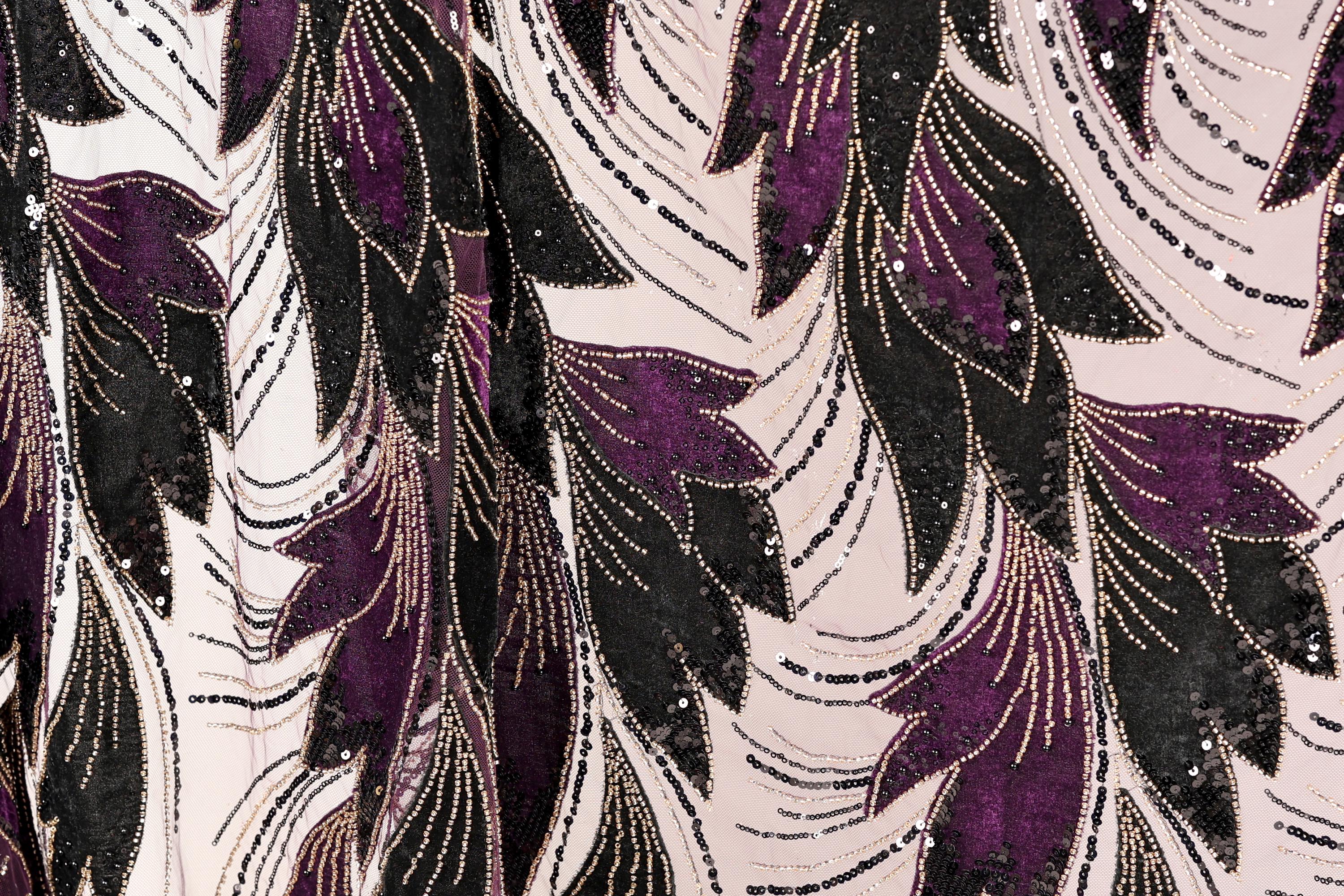 a close-up view of a fabric with a repeating pattern of purple and black leaves, accented with gold sequins. The pattern is intricate and detailed, creating a visually striking and textured appearance.
