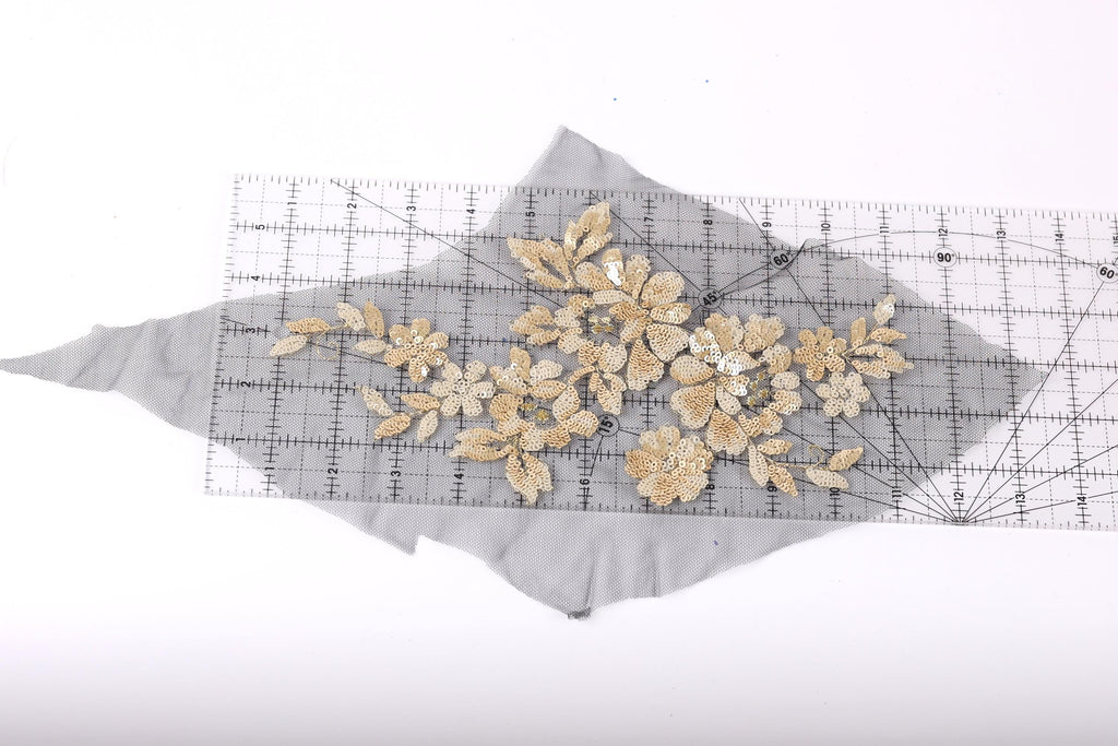 a close-up view of a piece of fabric with a floral pattern, including gold and white flowers, placed on a ruler.