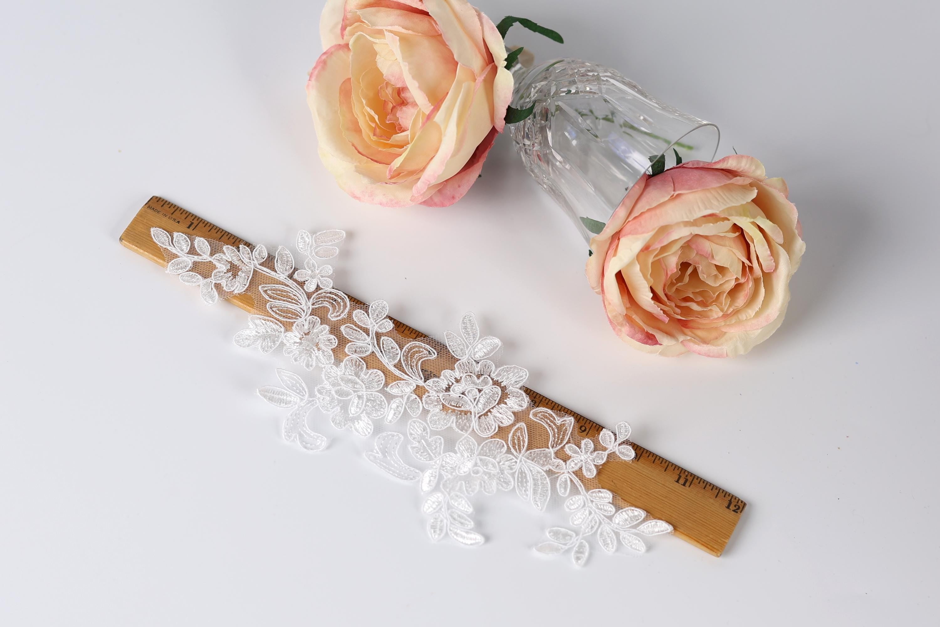 a lace piece, a wooden ruler, and two pink roses on a white background.