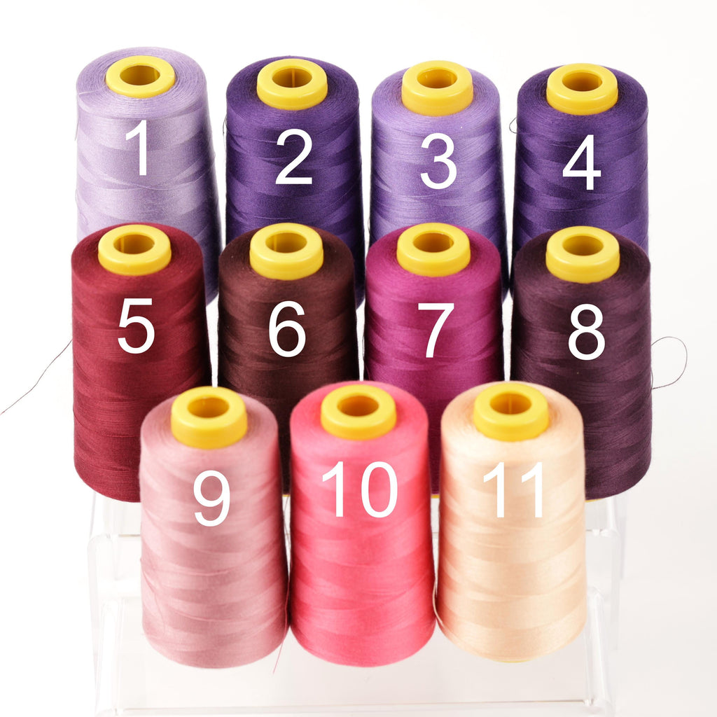 A collection of nine spools of thread in various colors, including purple, pink, and yellow, arranged in a grid-like pattern.