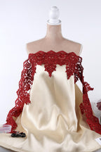 A mannequin wearing a white dress with red lace detailing and a red bow on the neckline.