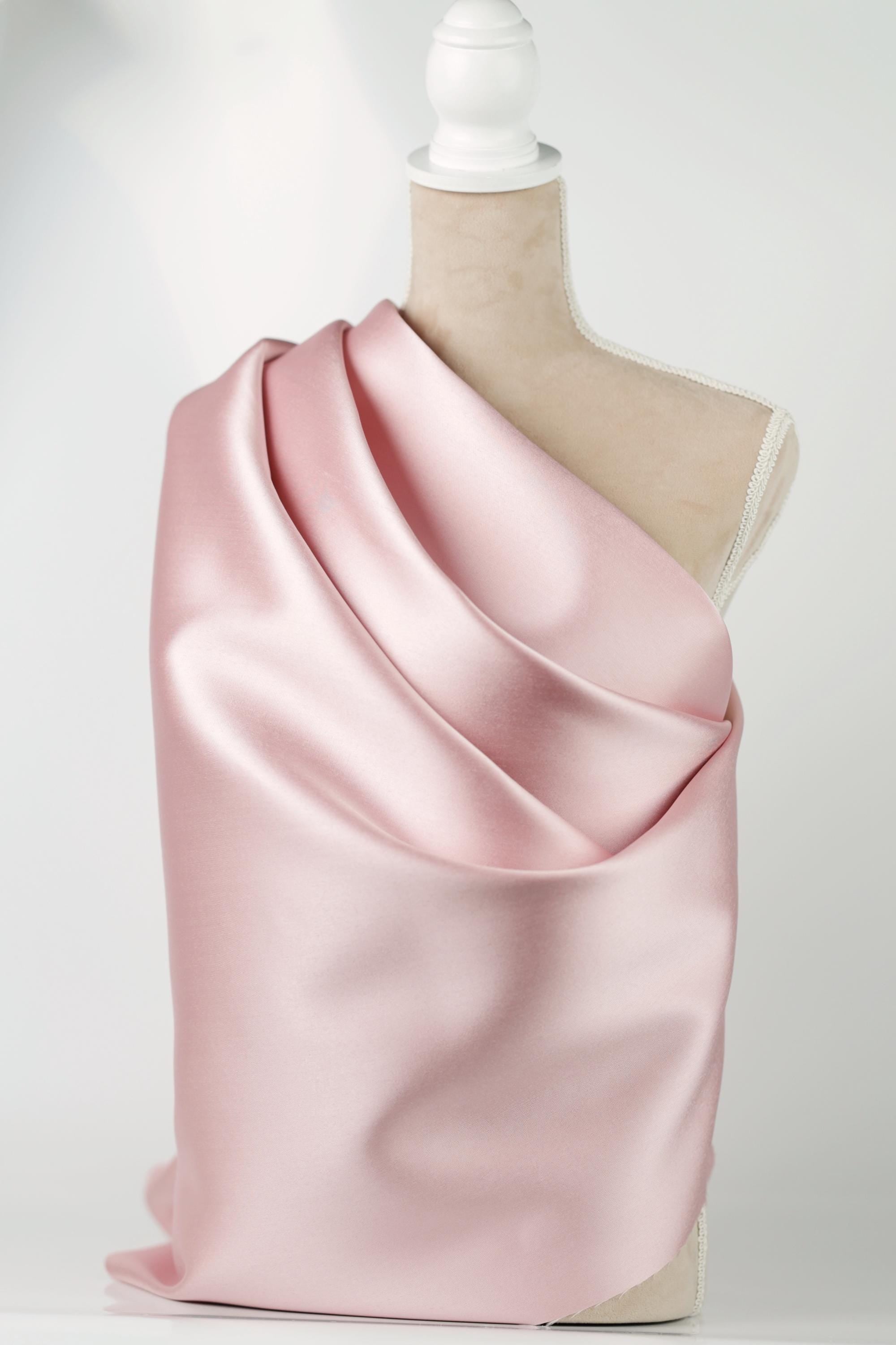 A mannequin is wearing a pink satin fabric draped over its shoulder.