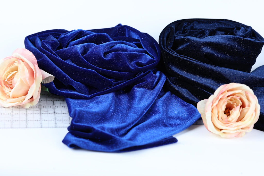 a close-up view of two fabric swatches, one blue and one black, with a single pink rose resting on the left side.