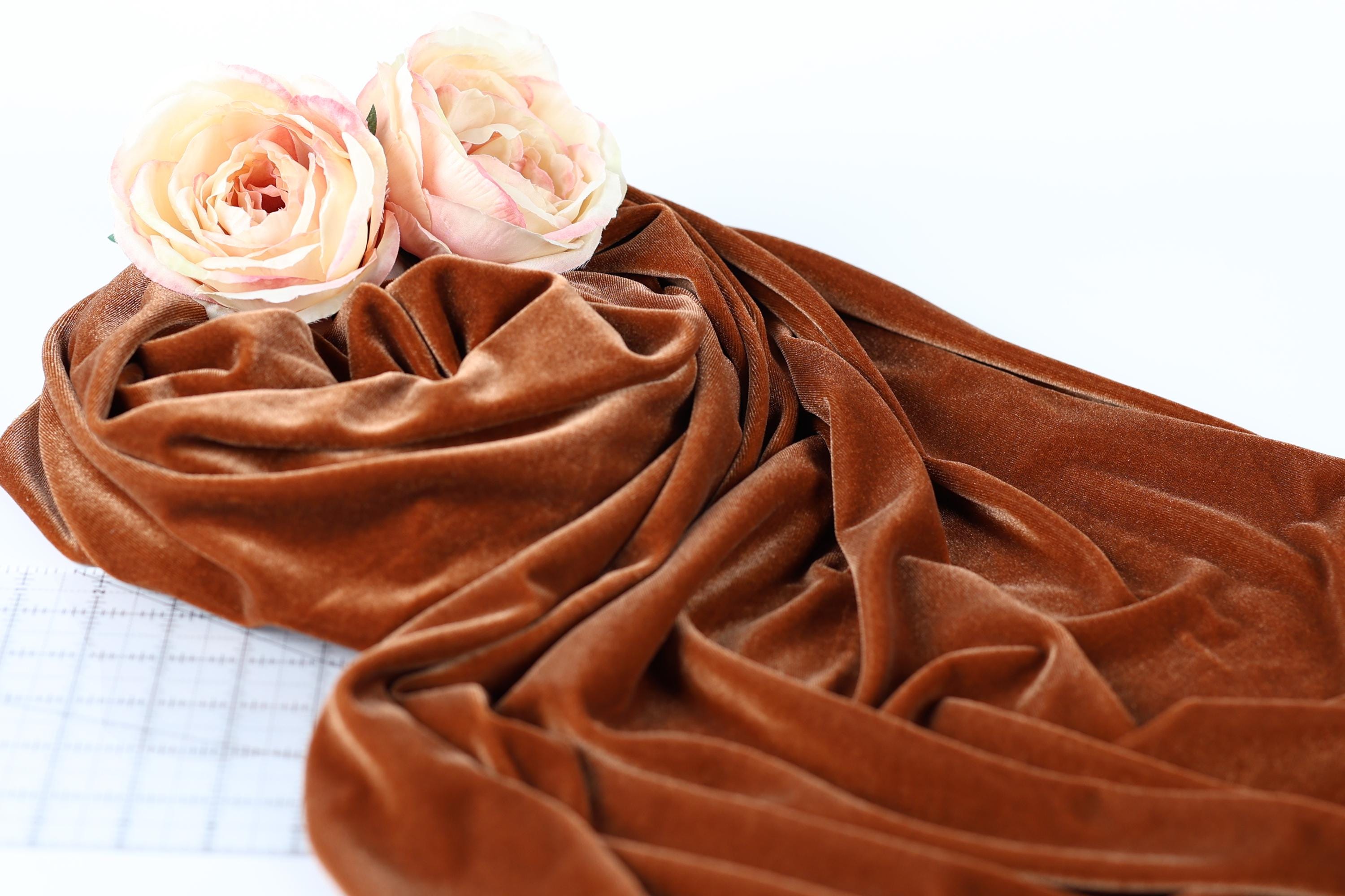 two pink roses resting on a crumpled brown fabric.