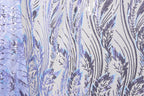 a close-up view of a fabric with a repeating pattern of purple and blue sequin designs. The pattern consists of various lines and shapes, creating a visually striking and intricate design. The fabric appears to be a piece of clothing or textile, with the sequin designs adding a touch of sparkle and texture to the overall appearance.