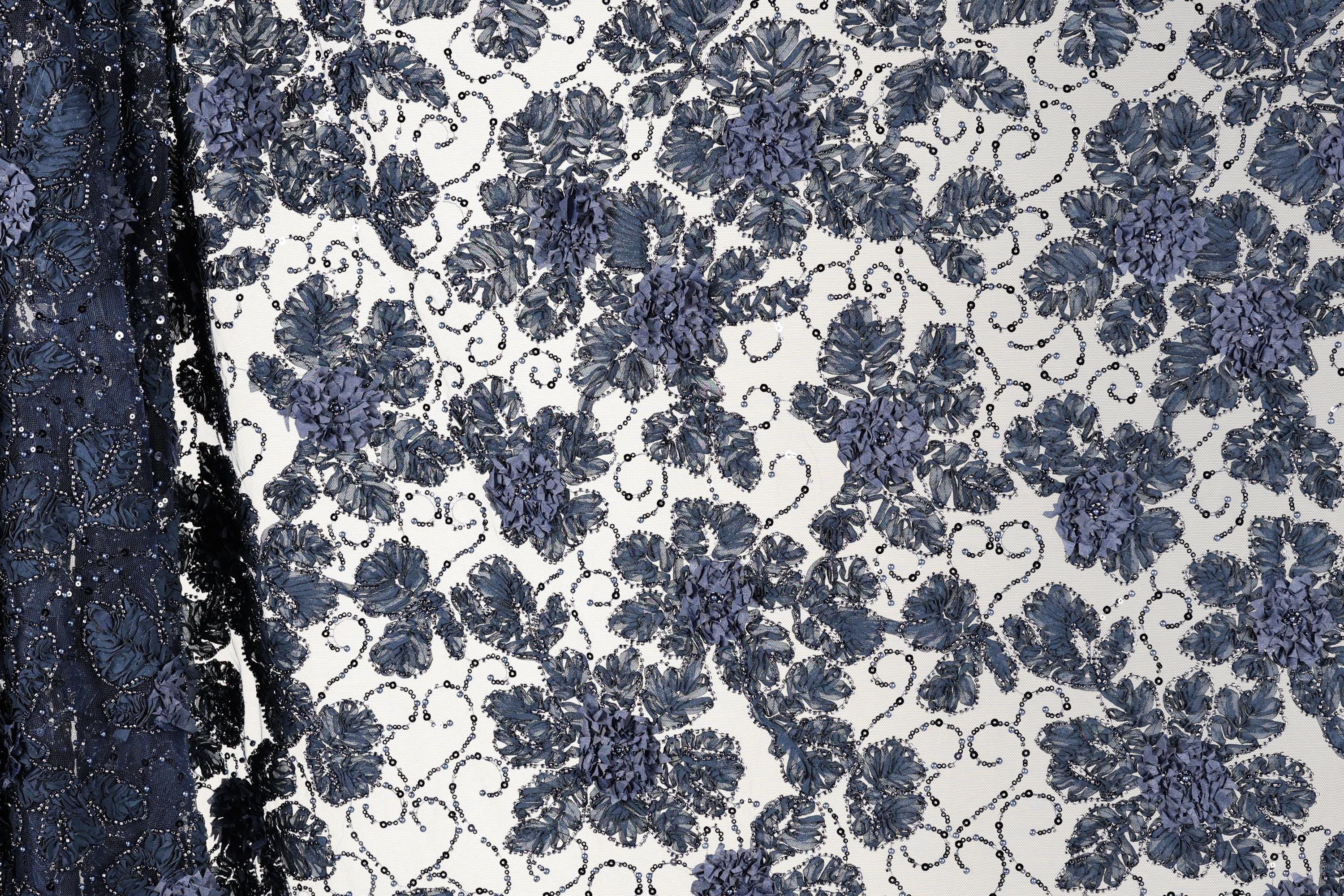 a close-up view of a fabric with a floral pattern in shades of blue and white. The fabric appears to be a lace or a similar type of textile, with a repeating floral design that creates a visually striking pattern.