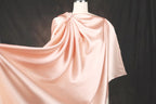 A mannequin wearing a flowing, draped pink satin garment against a dark background.