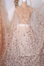 a mannequin wearing a dress with a delicate, leaf-like pattern in shades of peach and beige. The dress appears to be made of sheer fabric, giving it a delicate and airy appearance.