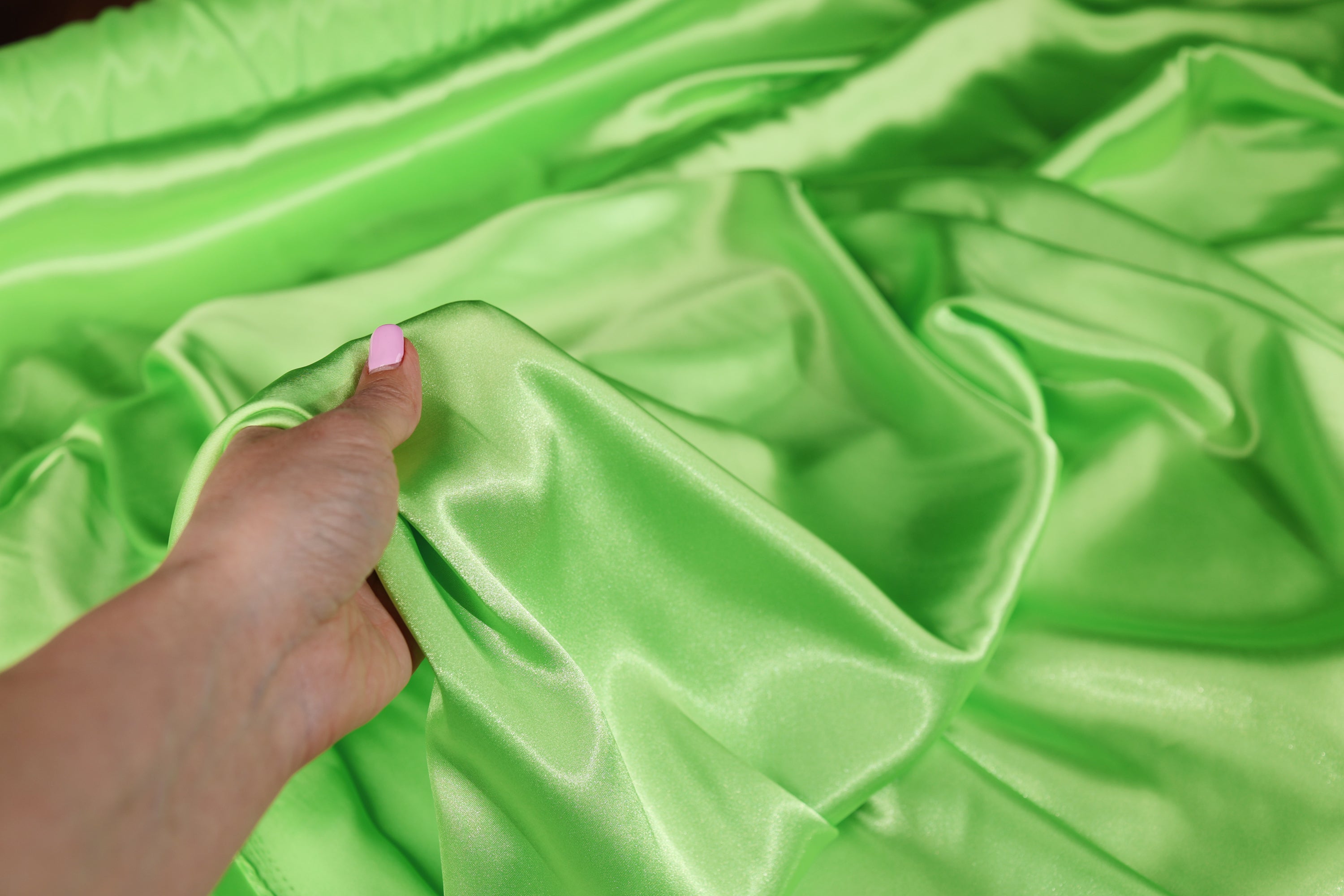 A hand is holding a piece of green satin fabric, examining it closely.