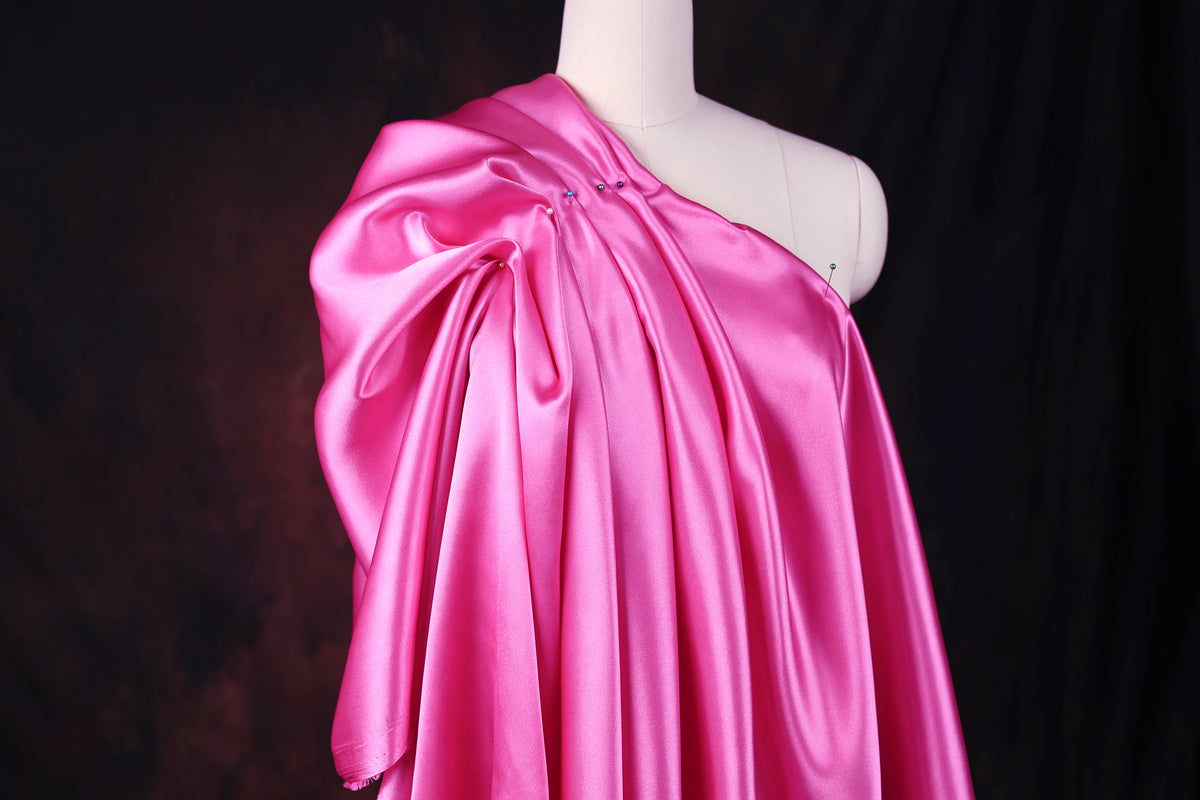 A mannequin wearing a bright pink satin one-shoulder dress against a dark background.