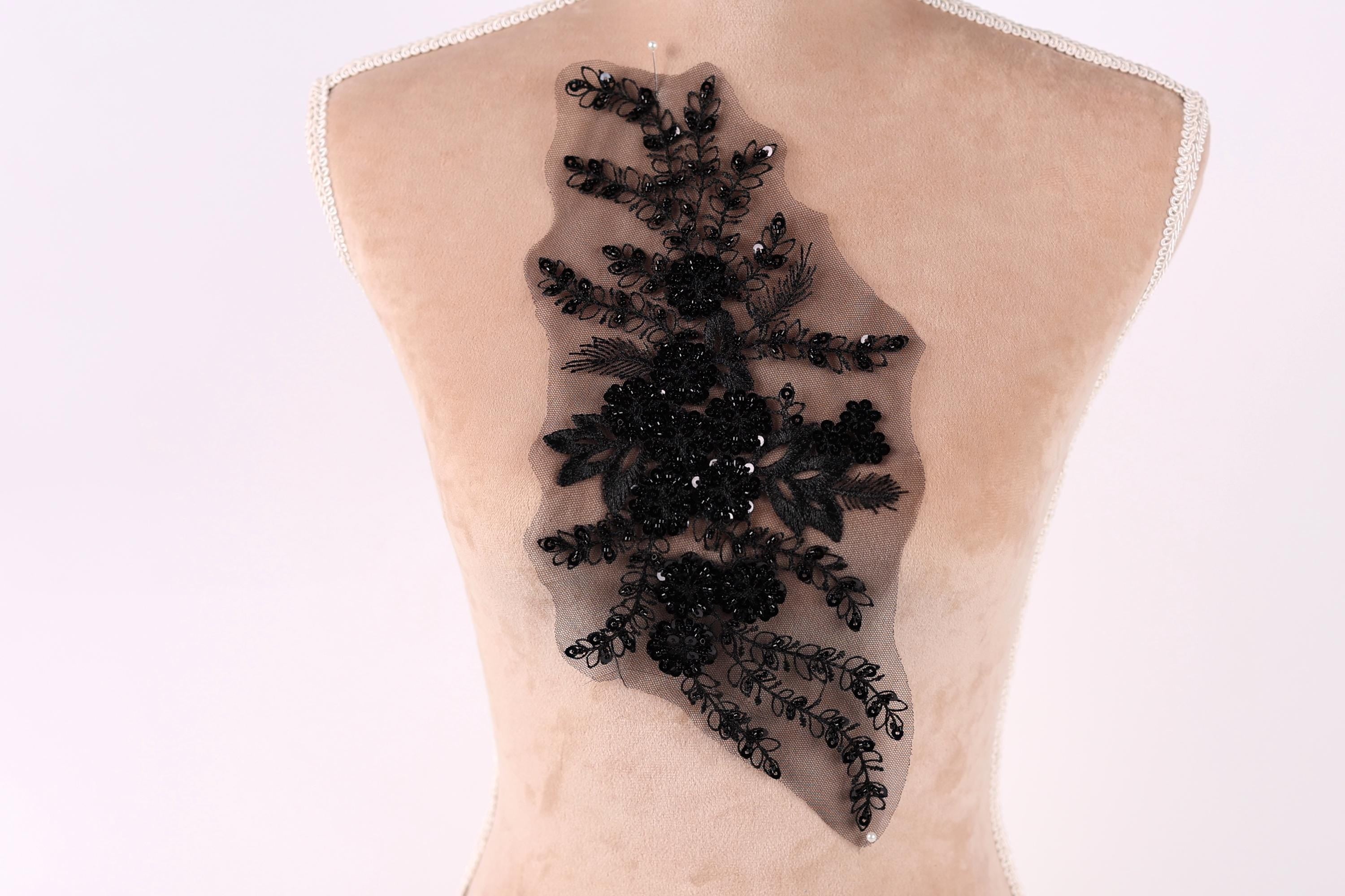 a mannequin torso with a decorative black lace or beaded floral pattern on the back.