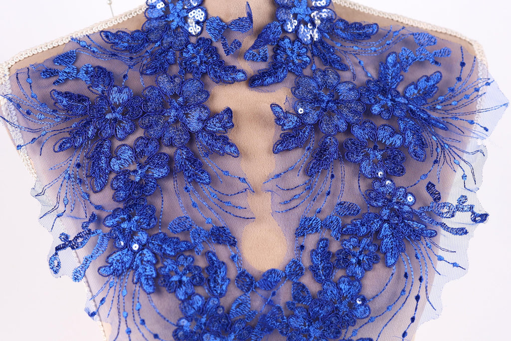 a close-up view of a delicate, intricate piece of blue lace or fabric adorned with a floral pattern. The lace appears to be hand-stitched, showcasing the craftsmanship and attention to detail in the design.