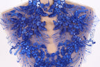 a close-up view of a delicate, intricate piece of blue lace or fabric adorned with a floral pattern. The lace appears to be hand-stitched, showcasing the craftsmanship and attention to detail in the design.