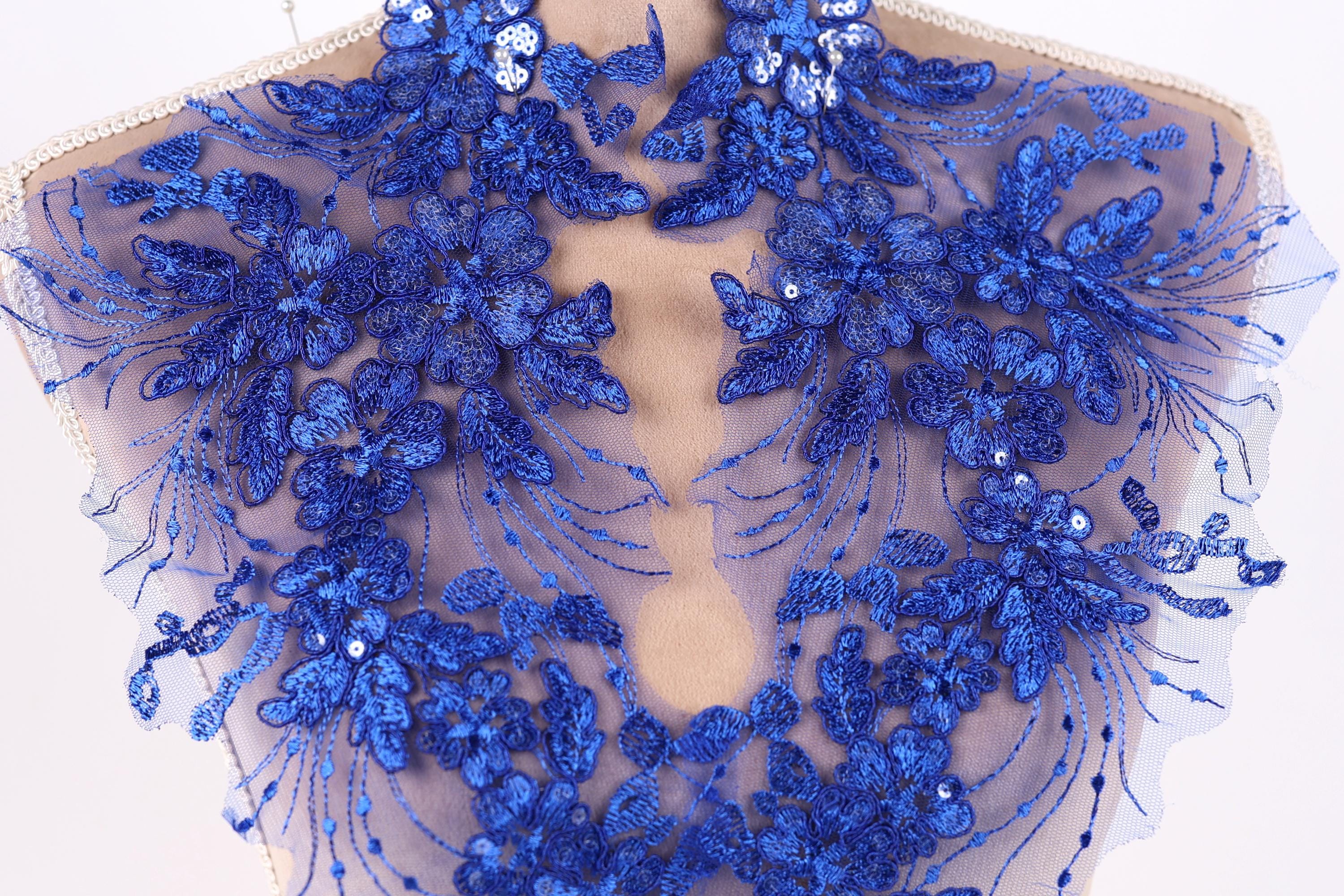 a close-up view of a delicate, intricate piece of blue lace or fabric adorned with a floral pattern. The lace appears to be hand-stitched, showcasing the craftsmanship and attention to detail in the design.
