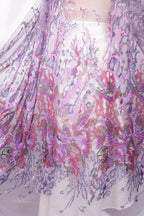 a close-up view of a fabric with a floral pattern in shades of purple and pink. The fabric appears to be made of sheer material, giving it a delicate and airy appearance. The intricate design and vibrant colors make the fabric visually appealing and eye-catching.