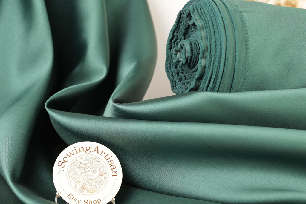 a close-up of a green satin fabric, with a rolled-up spool of the same material visible in the background. There is also a small white circular object with text on it placed in the foreground.